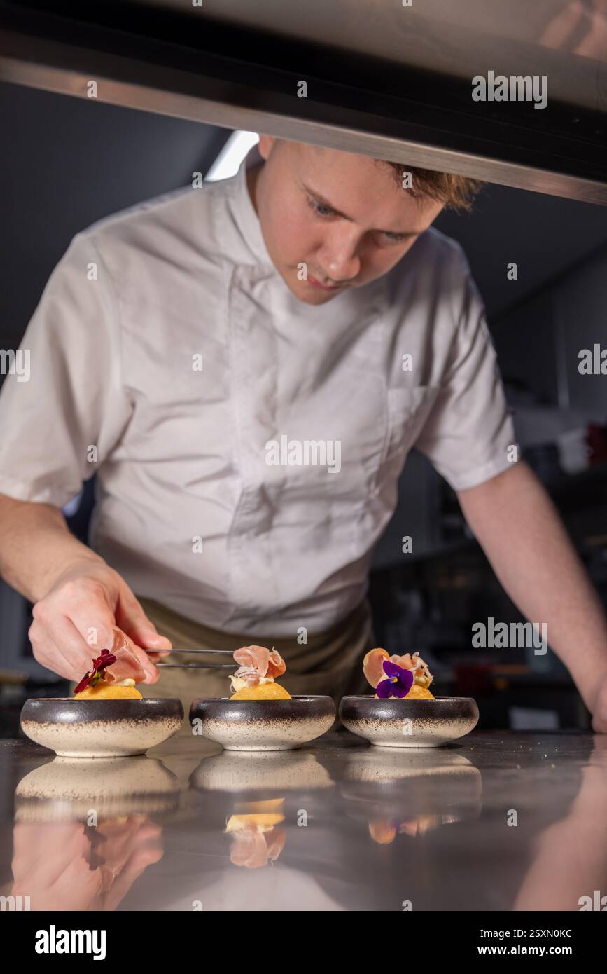 Küchenchef garniert Gourmetgerichte mit Blumen und Schinken in der Restaurantküche Stockfoto