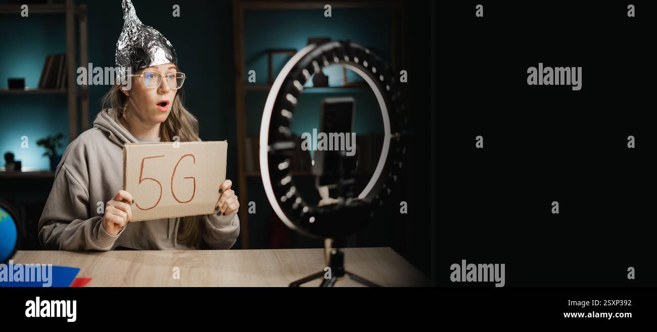 Seltsame Bloggerin in Folienhut, die 5G-Text zeigt, der mit ihren Abonnenten vor der Kamera spricht, und sie nimmt zu Hause Livestreams auf. Fake News und Verschwörung Stockfoto