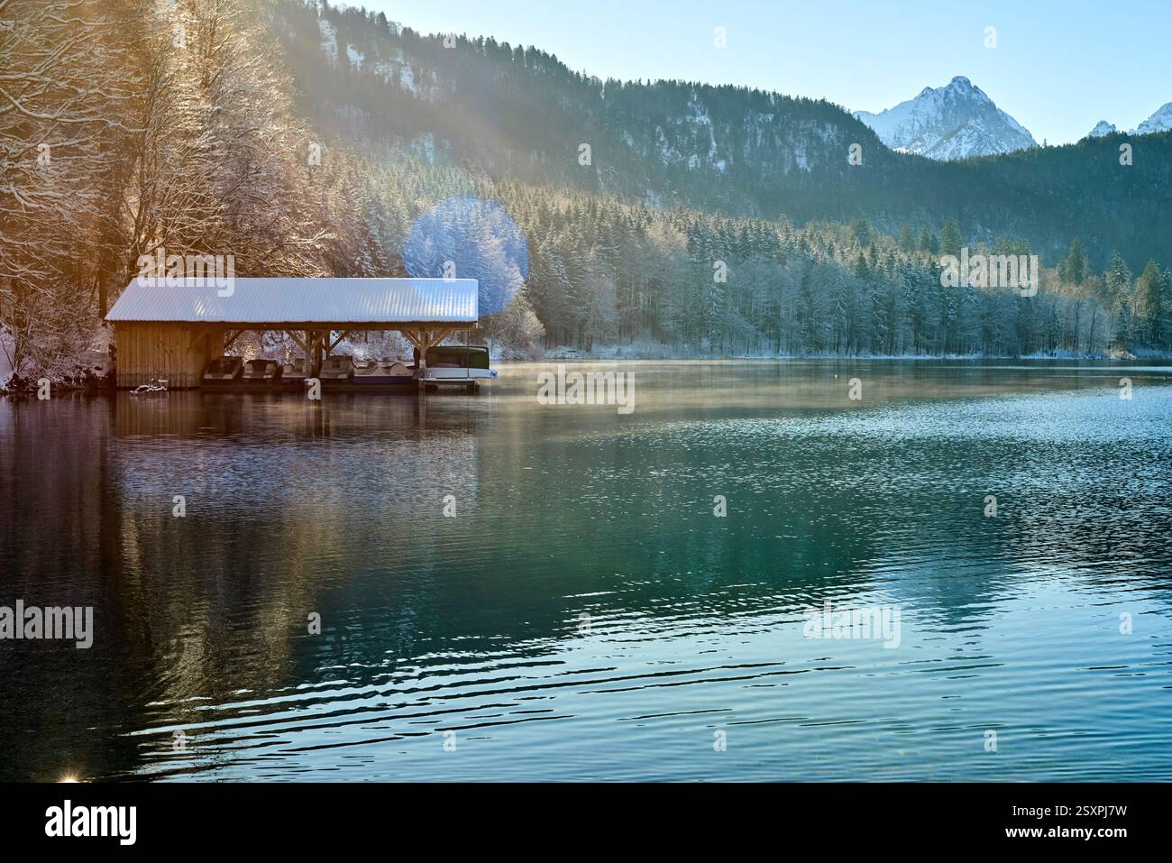 Dieses Foto zeigt eine ruhige Winterszene an einem ruhigen See. Das Bild zeigt ein hölzernes Dock, das in das Wasser hineinreicht und teilweise mit einem s bedeckt ist Stockfoto