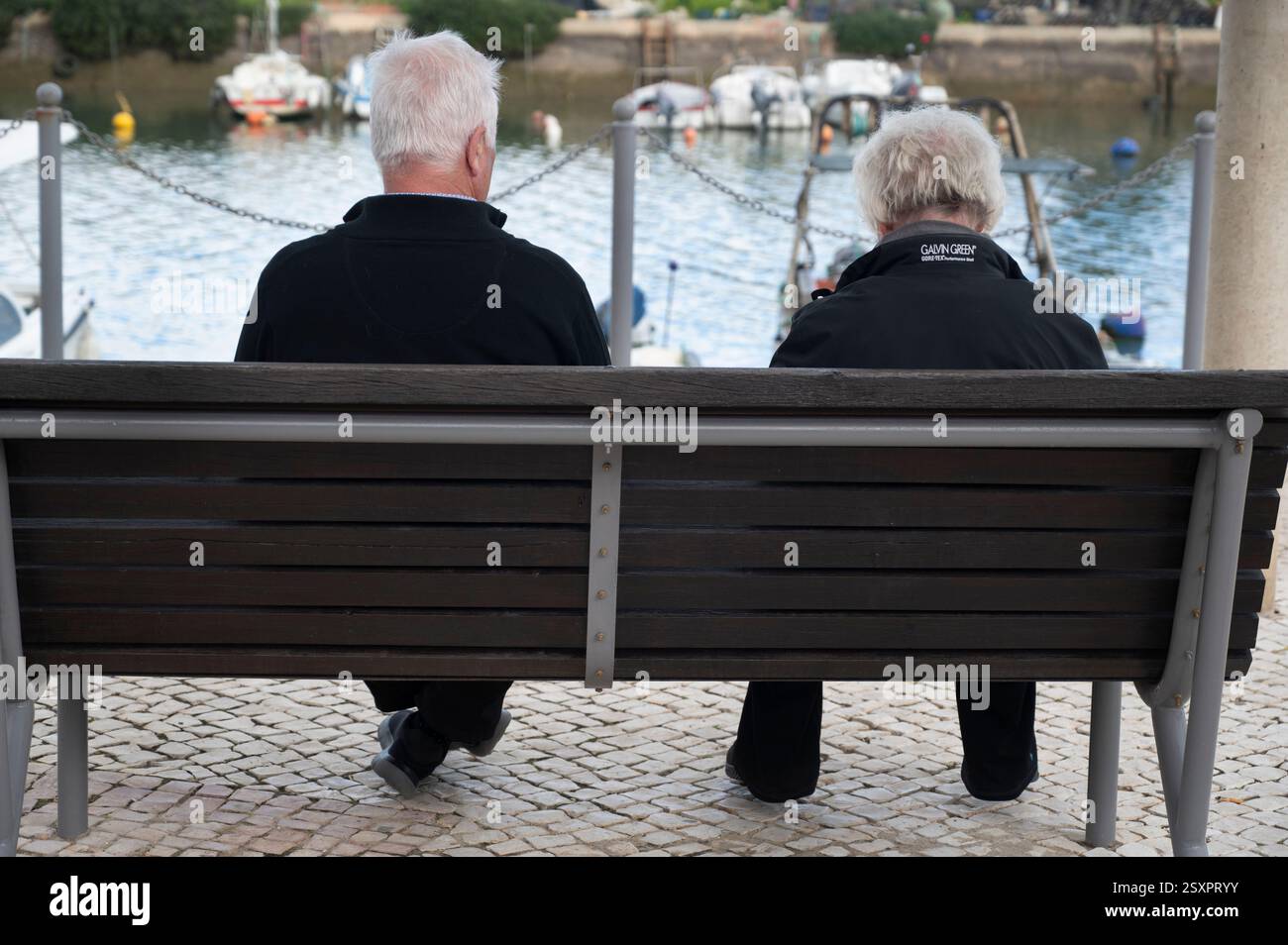 Portugal, Algarve; Fuseta. Ein älteres Paar auf einer Bank, das Boote auf dem Wasser ansieht. Stockfoto