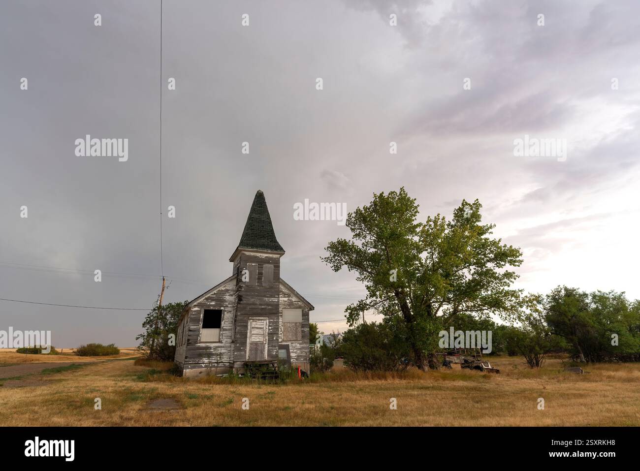 Verlassenes Kirchengebäude mit verschlossenen Fenstern und einem Turm, gelegen auf einem trockenen Grasfeld unter einem bewölkten Himmel, vermittelt ein Gefühl der Verlassenheit und Stockfoto