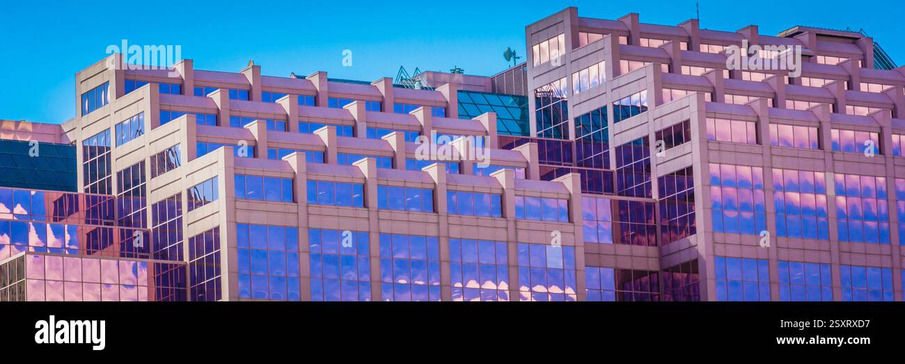 Großes Gebäude mit vielen Fenstern. Die Fenster sind klar und glänzend. Das Gebäude ist rosa. Der Himmel ist blau Stockfoto
