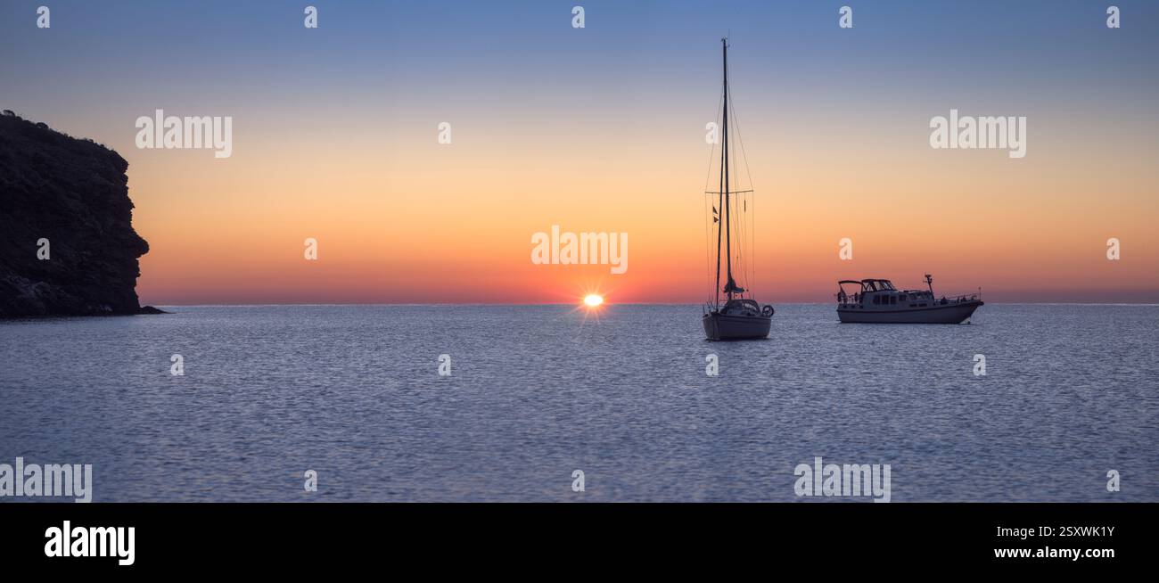Sanfte Wellen wallen, wenn die Sonne aufgeht und goldene Farbtöne auf dem ruhigen Wasser der Cala Joncols in Roses, Katalonien, ausstrahlen. Stockfoto