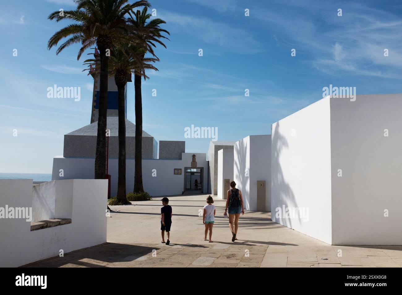 Familienspaziergang in der Nähe üppiger Palmen und eines modernen weißen Gebäudes unter dem blauen Himmel Stockfoto