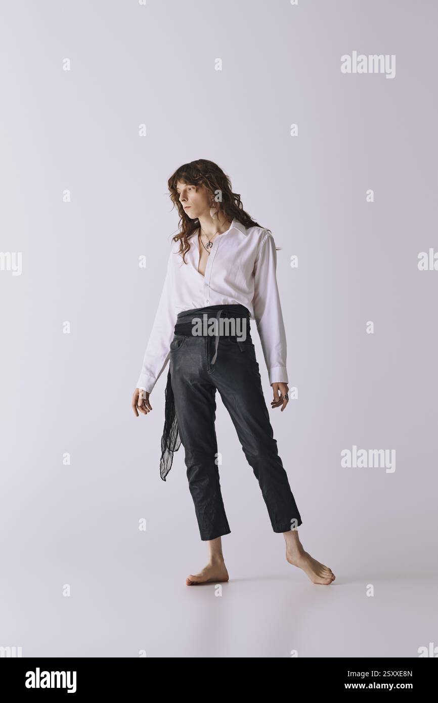Ein junger Mann mit modischem Look steht barfuß in einem schlanken, minimalistischen Studio und strahlt Selbstvertrauen aus. Stockfoto