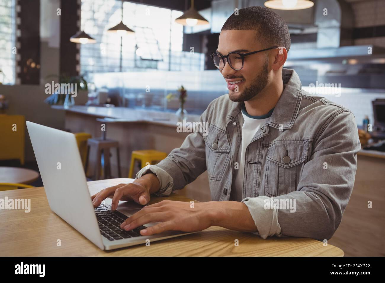 Lächelnder Mann, der in einem trendigen Café mit Laptop arbeitet und produktive Arbeitssitzungen genießt Stockfoto