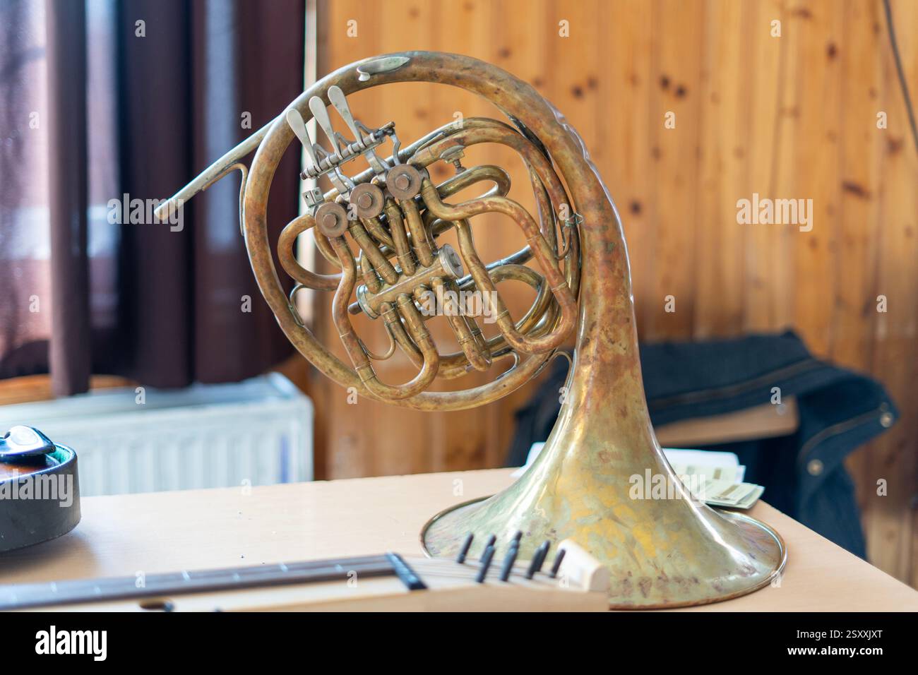 Ein französisches Horn aus Messing mit abgenutzter Patina liegt auf einem Holztisch in gemütlicher Atmosphäre. Stockfoto