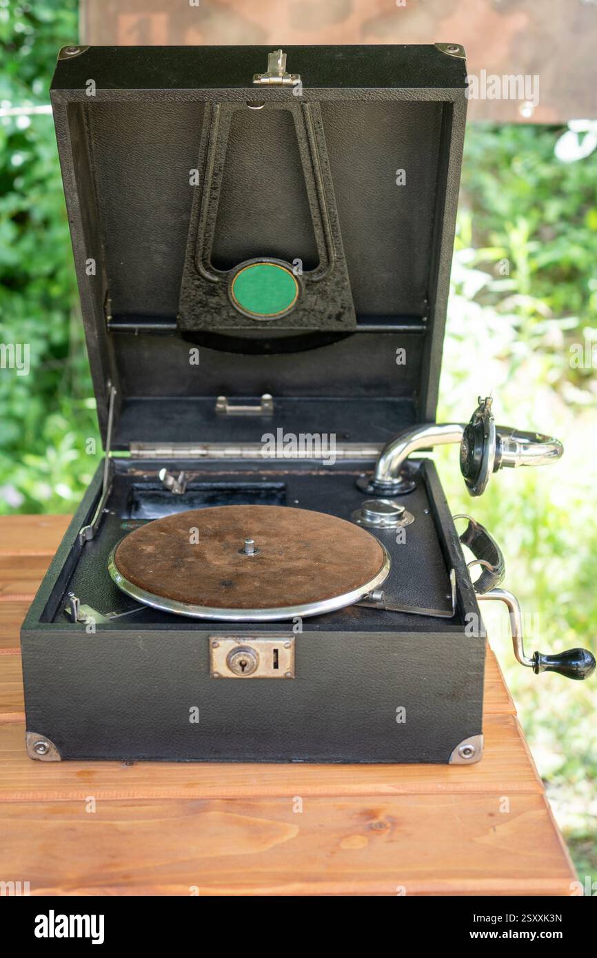 Ein klassisches tragbares Grammophon mit schwarzer Schallplatte wird auf einem Holztisch ausgestellt. Stockfoto
