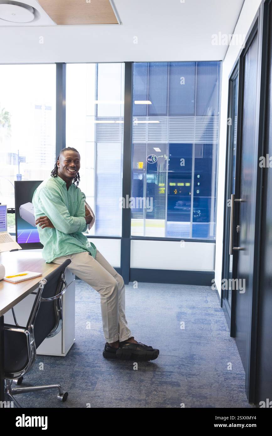 Lächelnder Mann im Büro, lehnt sich auf den Schreibtisch, genießt entspannte Arbeitsumgebung, Kopierraum Stockfoto