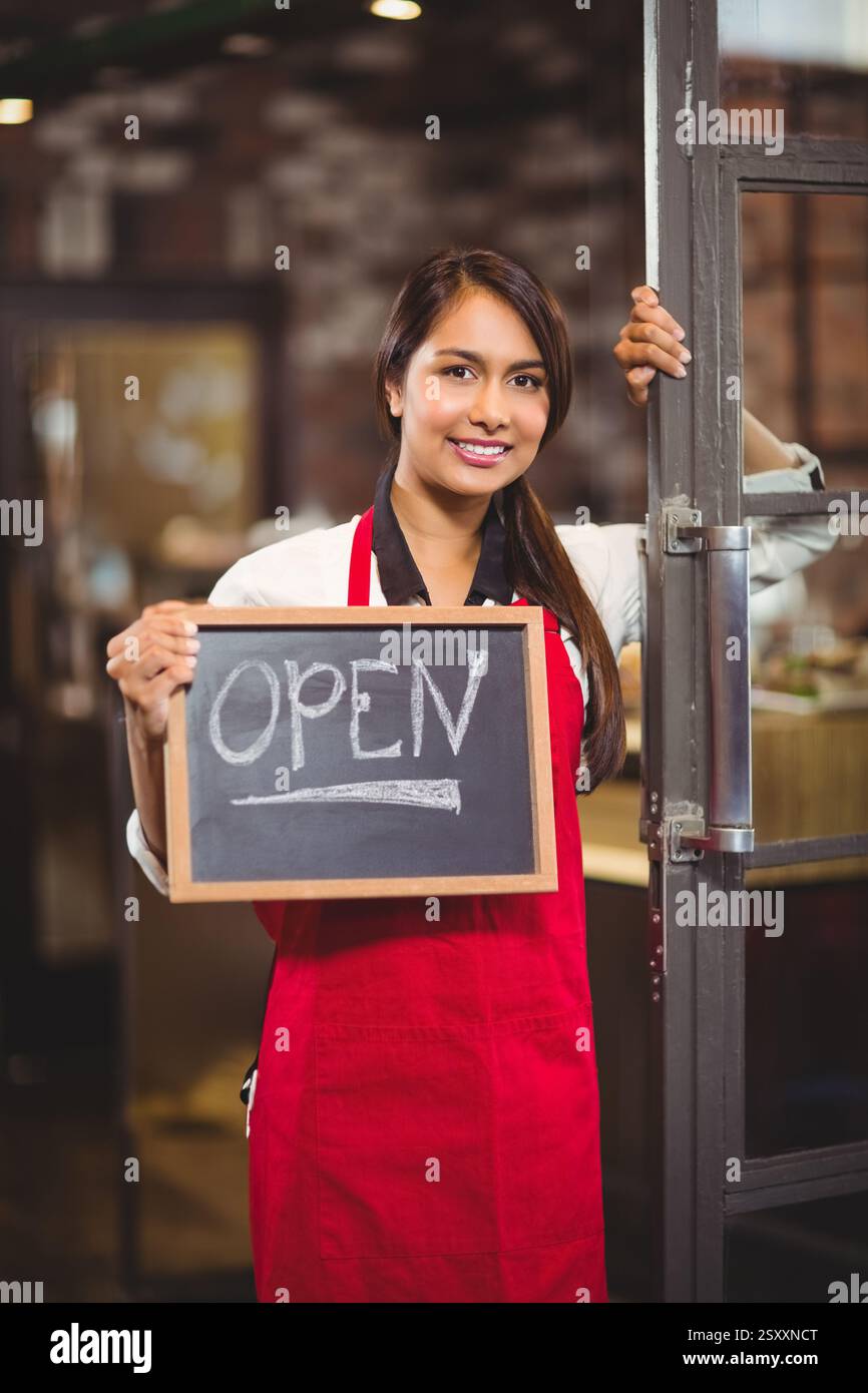 Lächelnde Frau auf roter Schürze mit offenem Schild am Eingang des Cafés Stockfoto