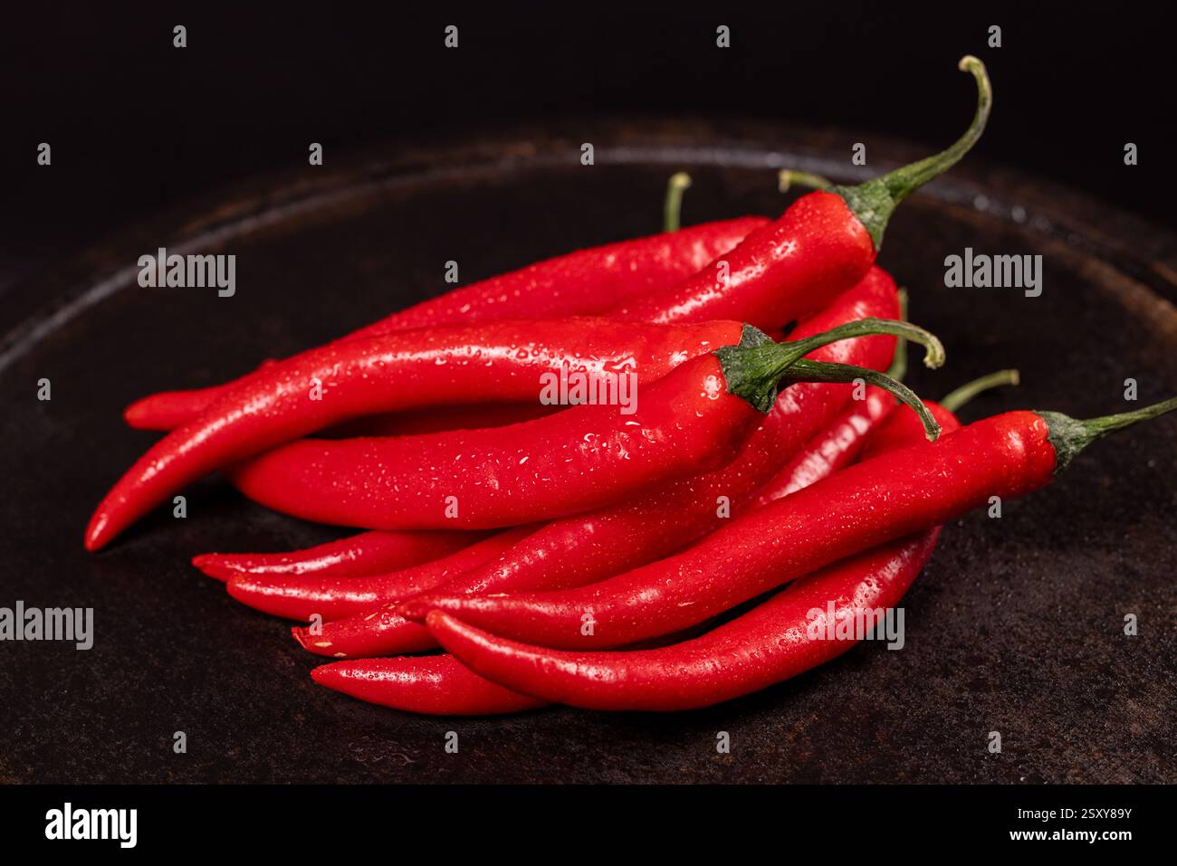 Leuchtend rote Chilischoten glitzern mit Wassertröpfchen, die auf einer dunklen Oberfläche aufgehäuft sind und ein beeindruckendes Bild von Frische und Würze schaffen Stockfoto