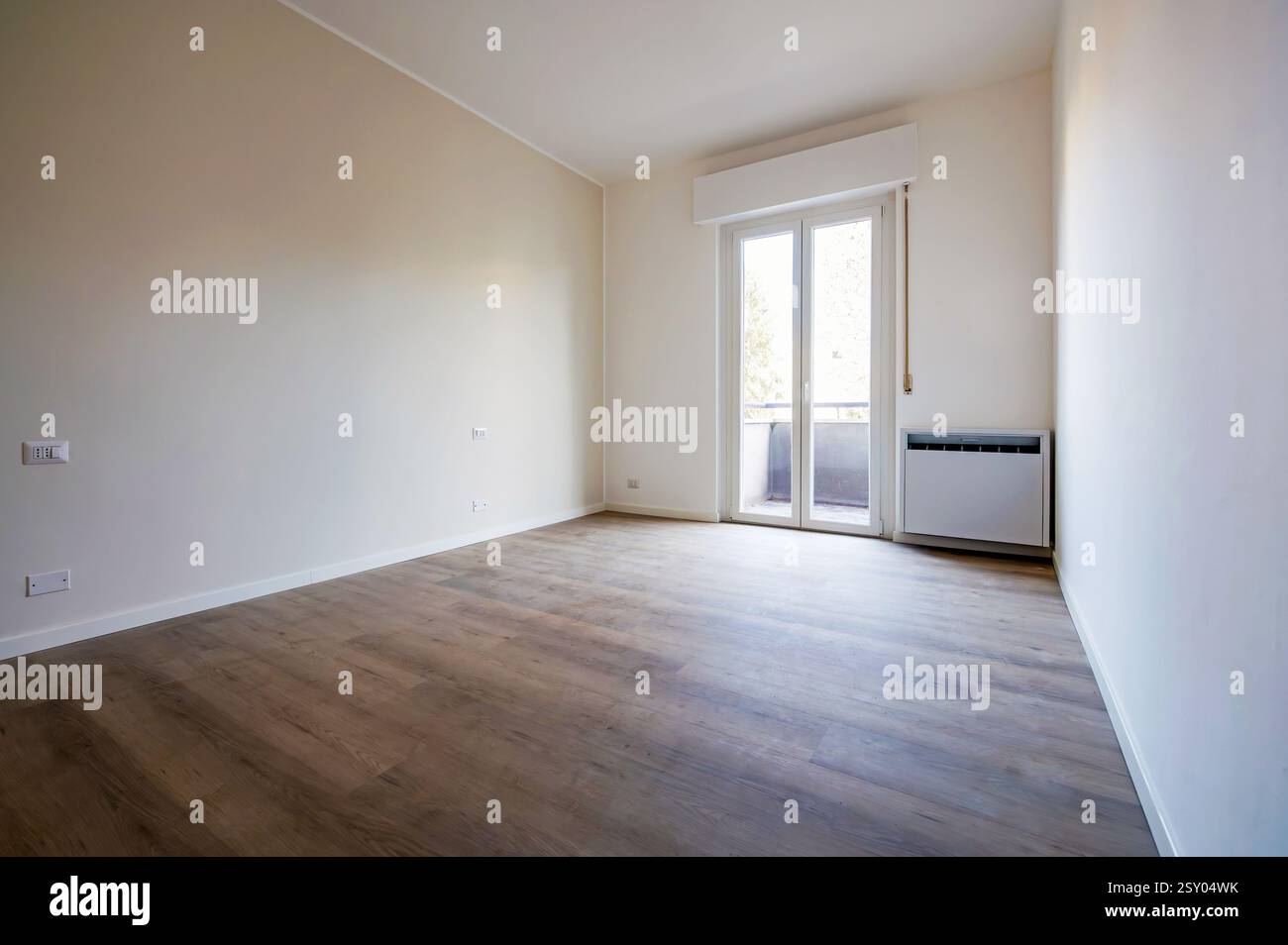 Leeres Apartment mit Holzboden, weißen Wänden, Balkontür und Heizkörper, ideal für Renovierungs- oder Innenarchitekturprojekte Stockfoto