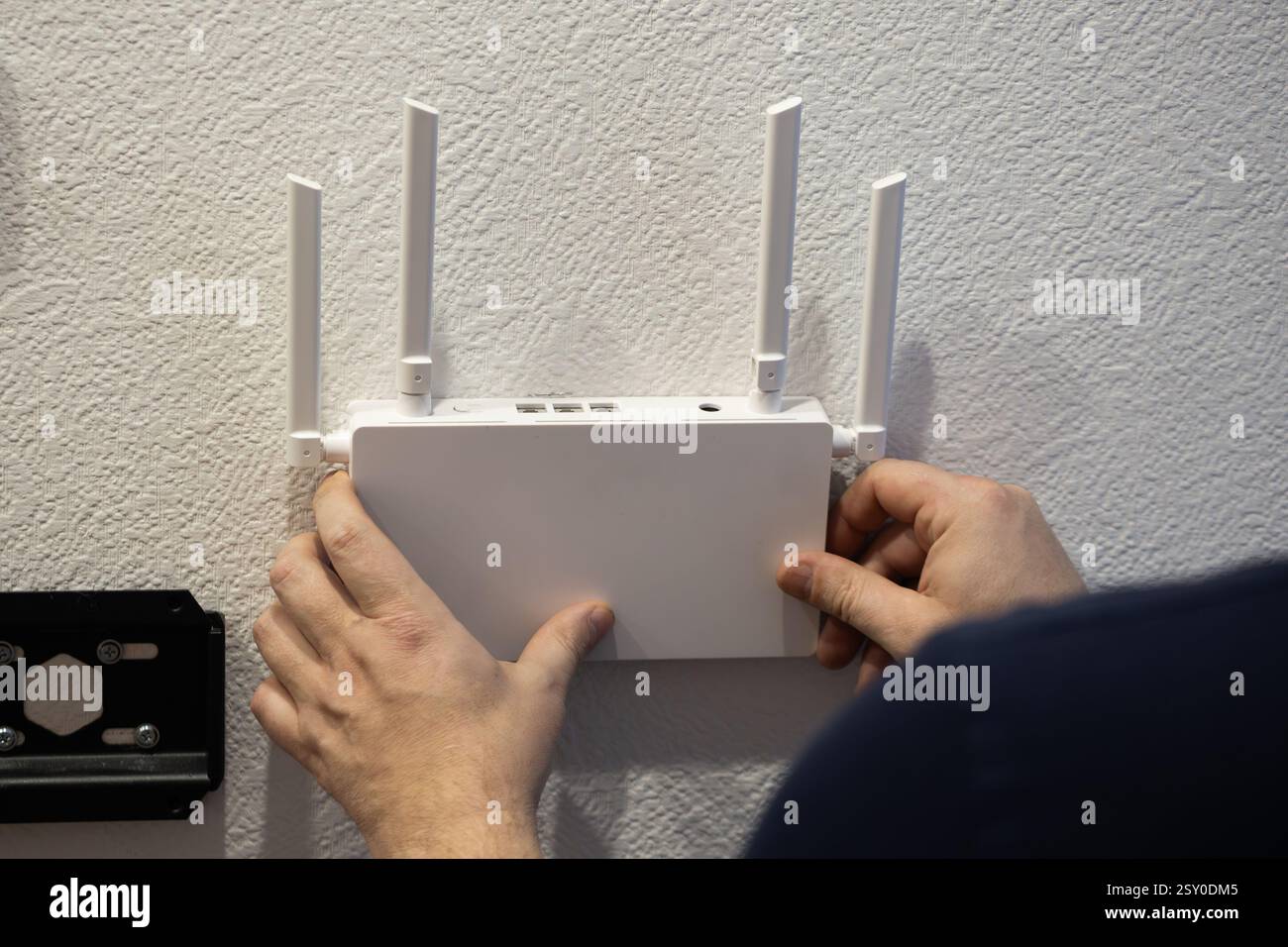 Eine Person installiert einen WLAN-Router mit Antennen an einer Wand, um den Internetzugang und die Konnektivität zu verbessern Stockfoto