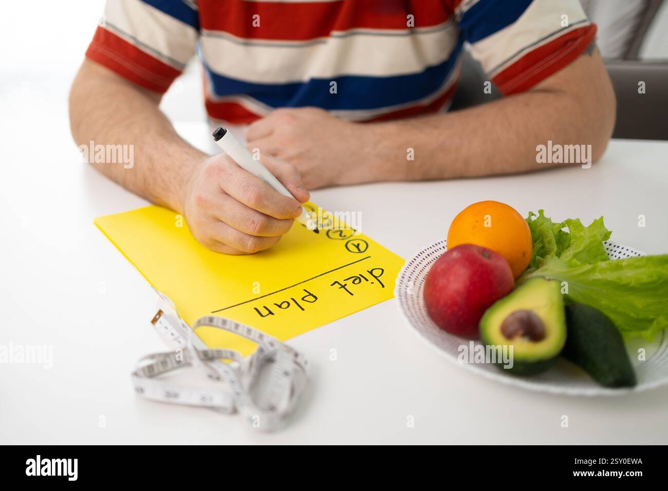 Eine Person erstellt einen nahrhaften Speiseplan mit gesunden Lebensmitteln und verwendet ein Maßband, um Portionen zu verfolgen Stockfoto