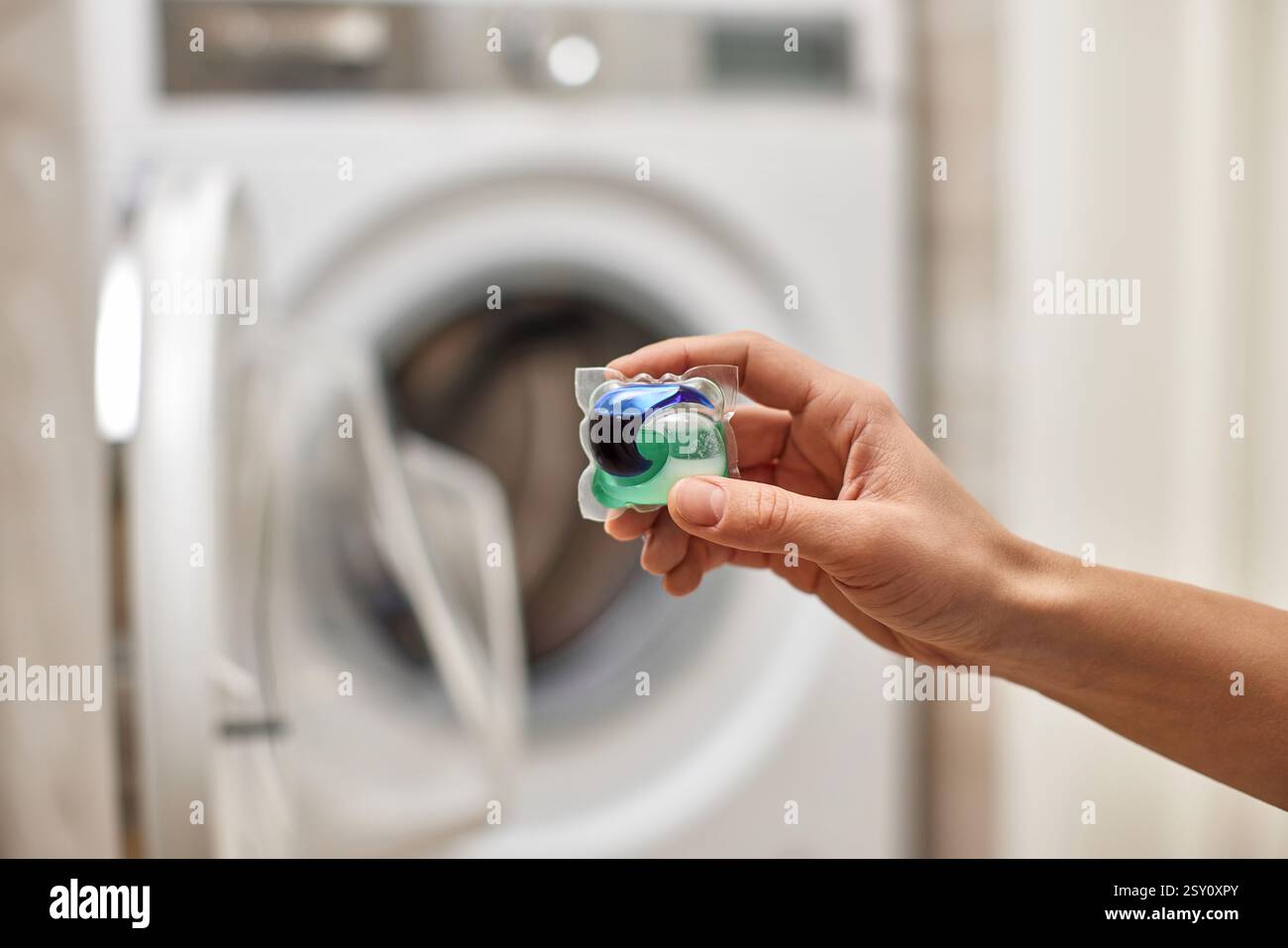 Weibliche Hand, die Waschmittelkapsel in die Waschmaschine gibt Stockfoto