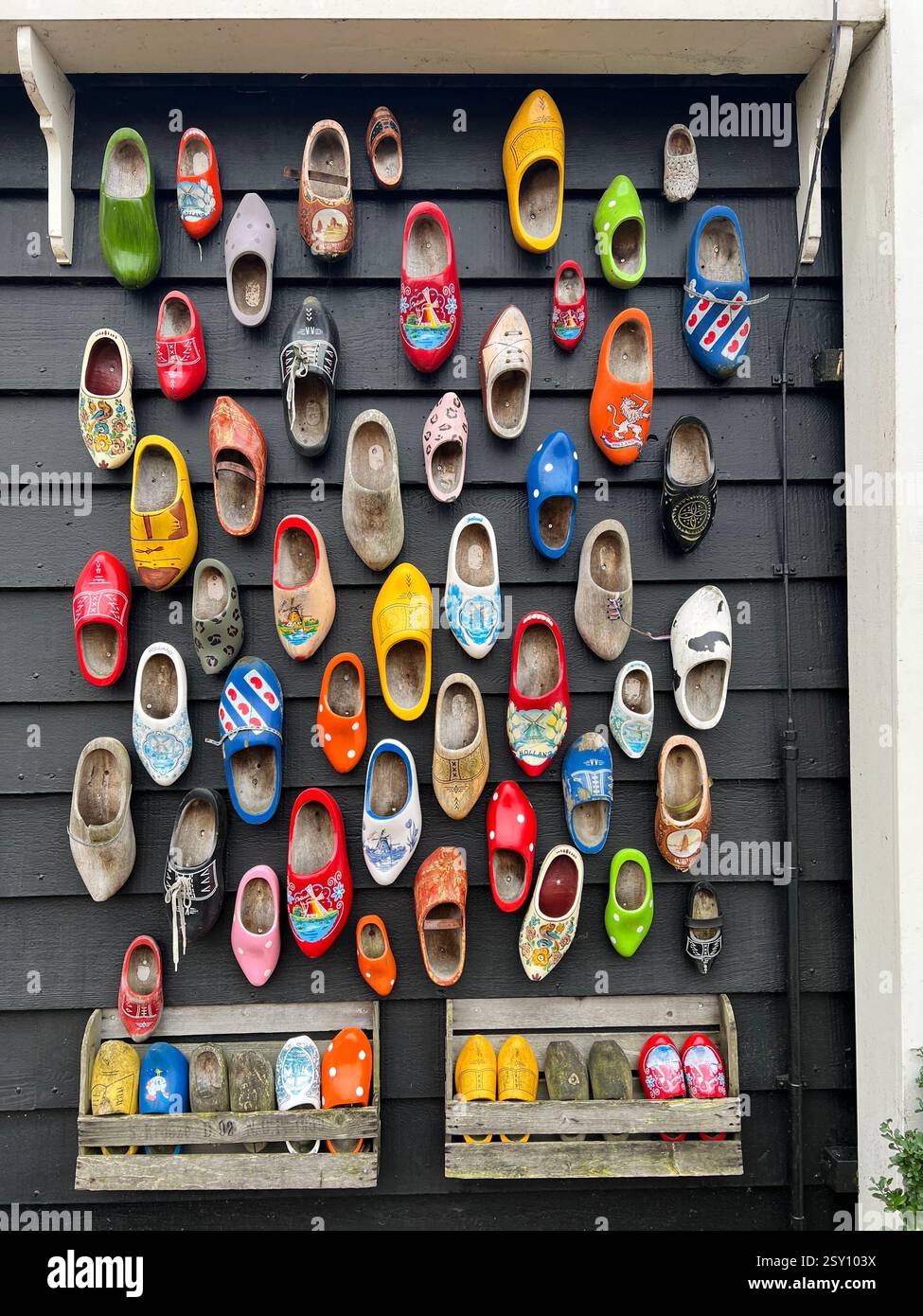 Eine lebendige Sammlung traditioneller holländischer Holzclogs, die auf einer schwarzen Holzwand montiert sind - Smartphone-aufgenommenes Stockfoto