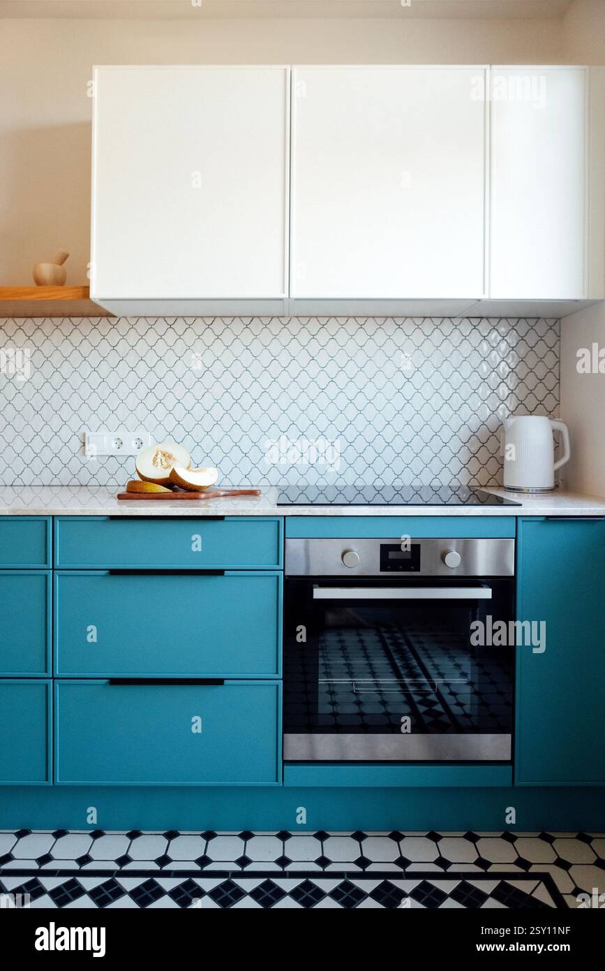 Eine moderne Küche mit blauem Set und Marmorarbeitsfläche. Offene Holzregale mit Küchenartikeln und stilvollen goldenen Lampen. Kaffeemaschine und geschnittenes mel Stockfoto