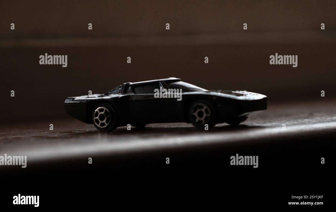 Schwarzes Miniatur-Spielzeugauto mit dramatischer Beleuchtung vor dunklem Hintergrund Stockfoto
