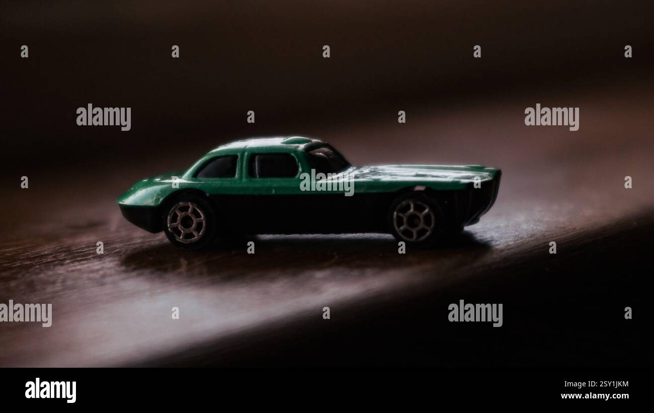Grüner Miniatur-Spielzeugwagen mit dramatischer Beleuchtung vor dunklem Hintergrund Stockfoto