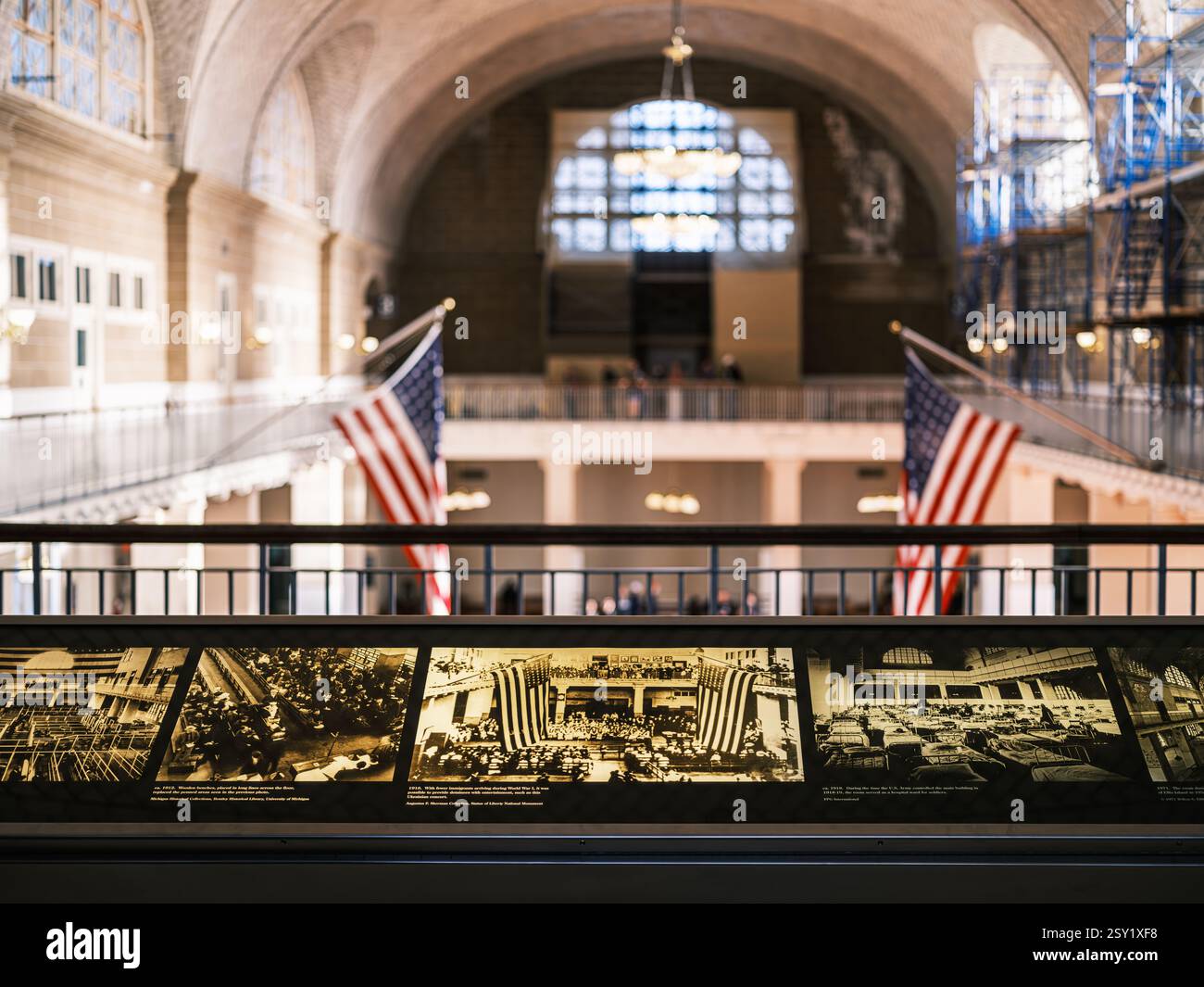 Blick von der obersten Etage von Ellis Island mit Informationstafeln, amerikanischen Flaggen, großer Architektur, einem Kronleuchter und Gerüsten während der Restaurierung. Stockfoto