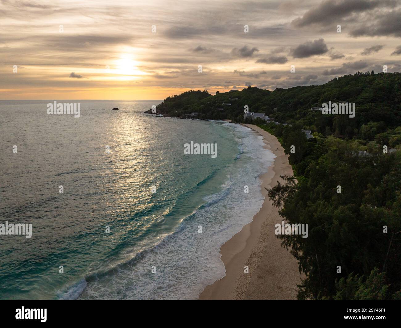 Die Sonne untergeht über einer ruhigen Küste mit sanften Wellen, die sich in goldenen Tönen spiegeln. Anse Intendance. Seychellen, Mahe. Stockfoto