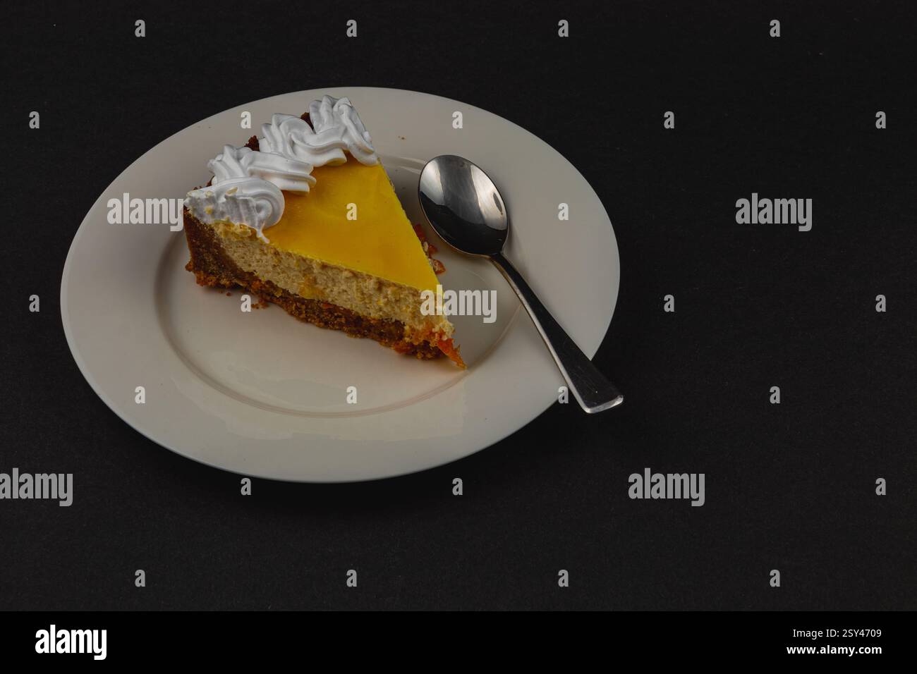 Ein samtiges Stück selbstgemachter Orangenkäsekuchen liegt auf einem Teller neben einem glänzenden Löffel und unterstreicht seine cremige Textur und das leuchtende Orange-Topping. Perfec Stockfoto