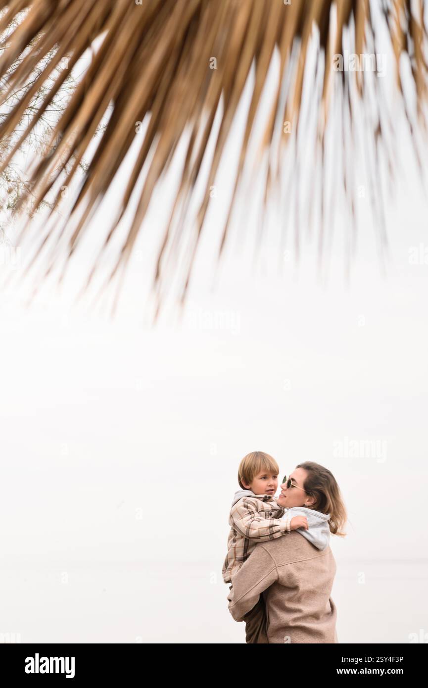 Mutter mit Sohn am Strand im Winter unter trockener Palme Stockfoto