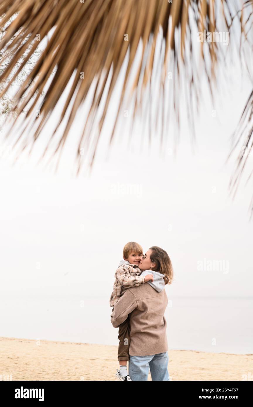 Mutter mit Sohn am Strand im Winter unter trockener Palme Stockfoto