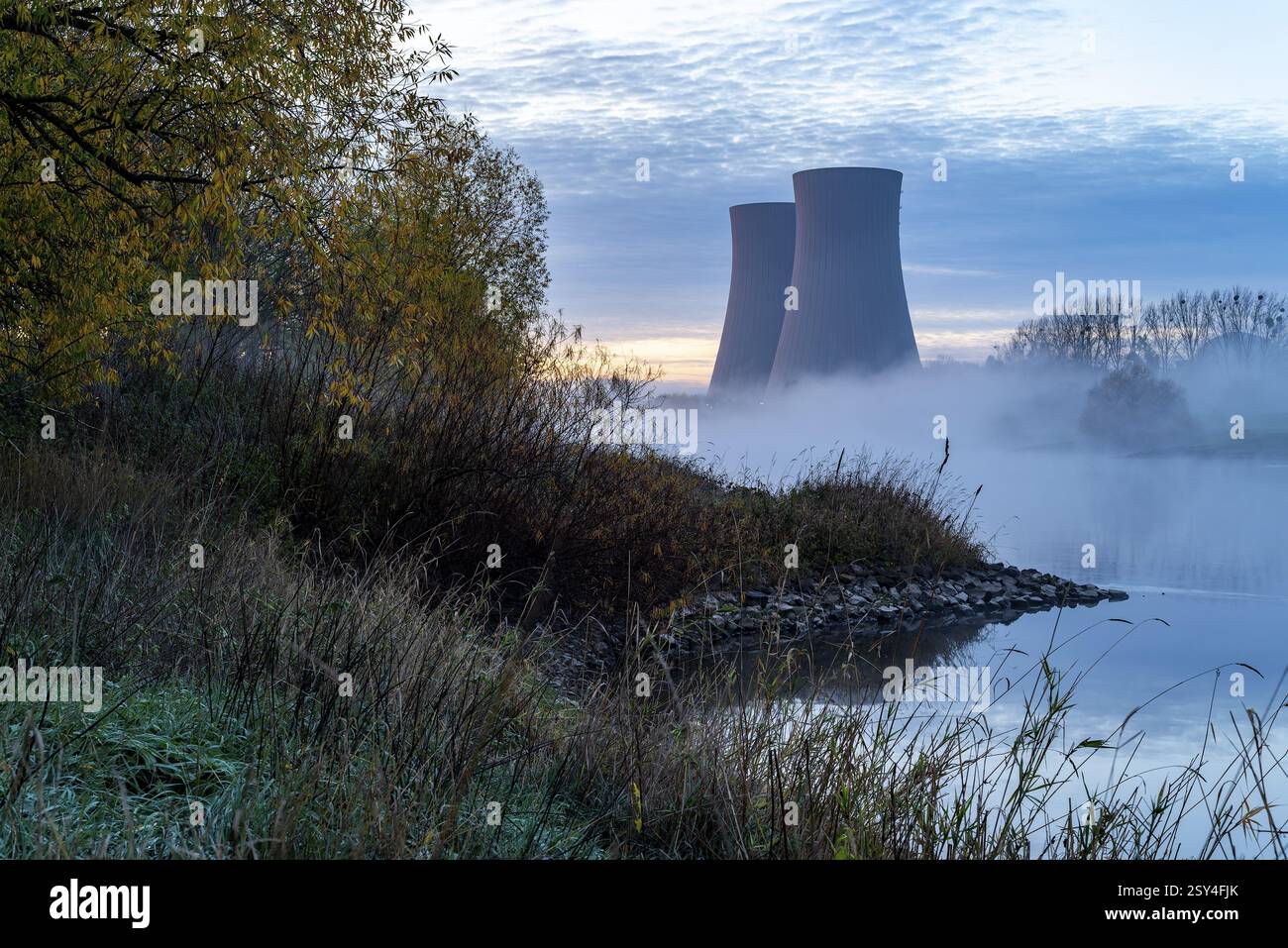 Kühltürme des Kernkraftwerks Grohne im Nebel am Morgen, umgeben von herbstlichem Weserufer und Bäumen, die ein Mysteri schaffen Stockfoto