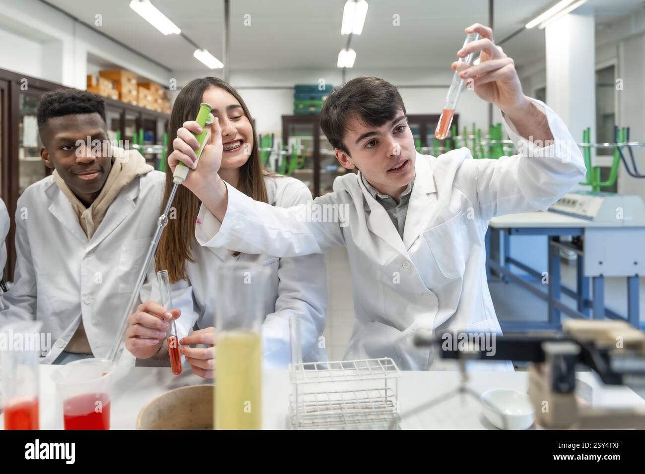 Junge Chemiestudenten, die Labormäntel tragen und Experimente mit Reagenzgläsern und anderen Laborgeräten durchführen Stockfoto