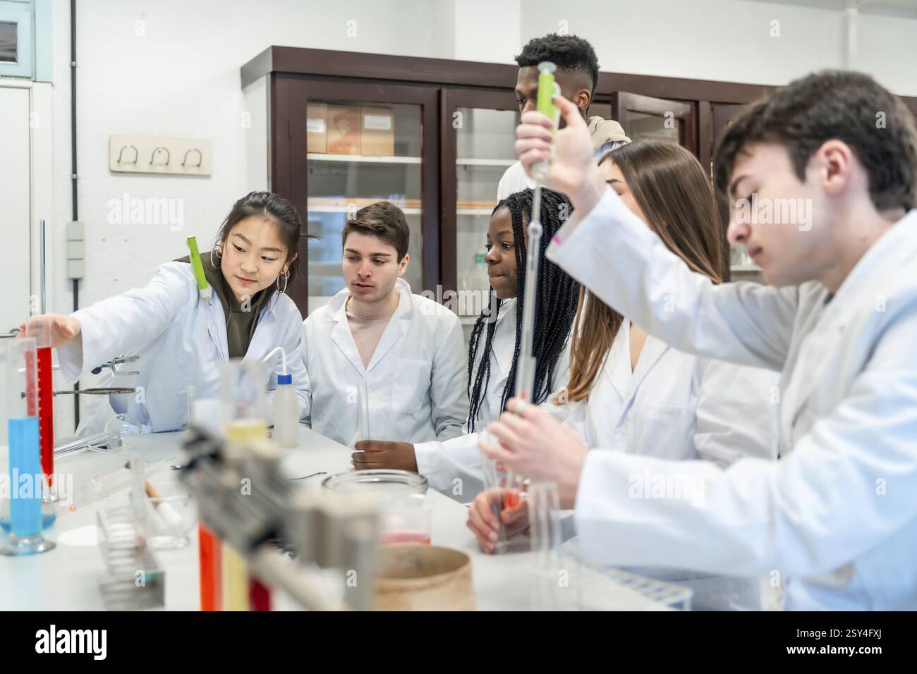 Universitätsstudenten in Laborkitteln, die ein Chemieexperiment mit bunten Flüssigkeiten und Laborgeräten durchführen Stockfoto
