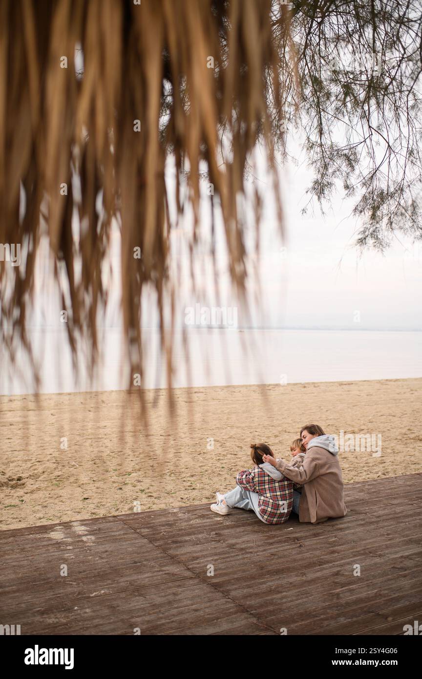 Mutter mit Kindern sitzt am Strand und umarmt sich Stockfoto