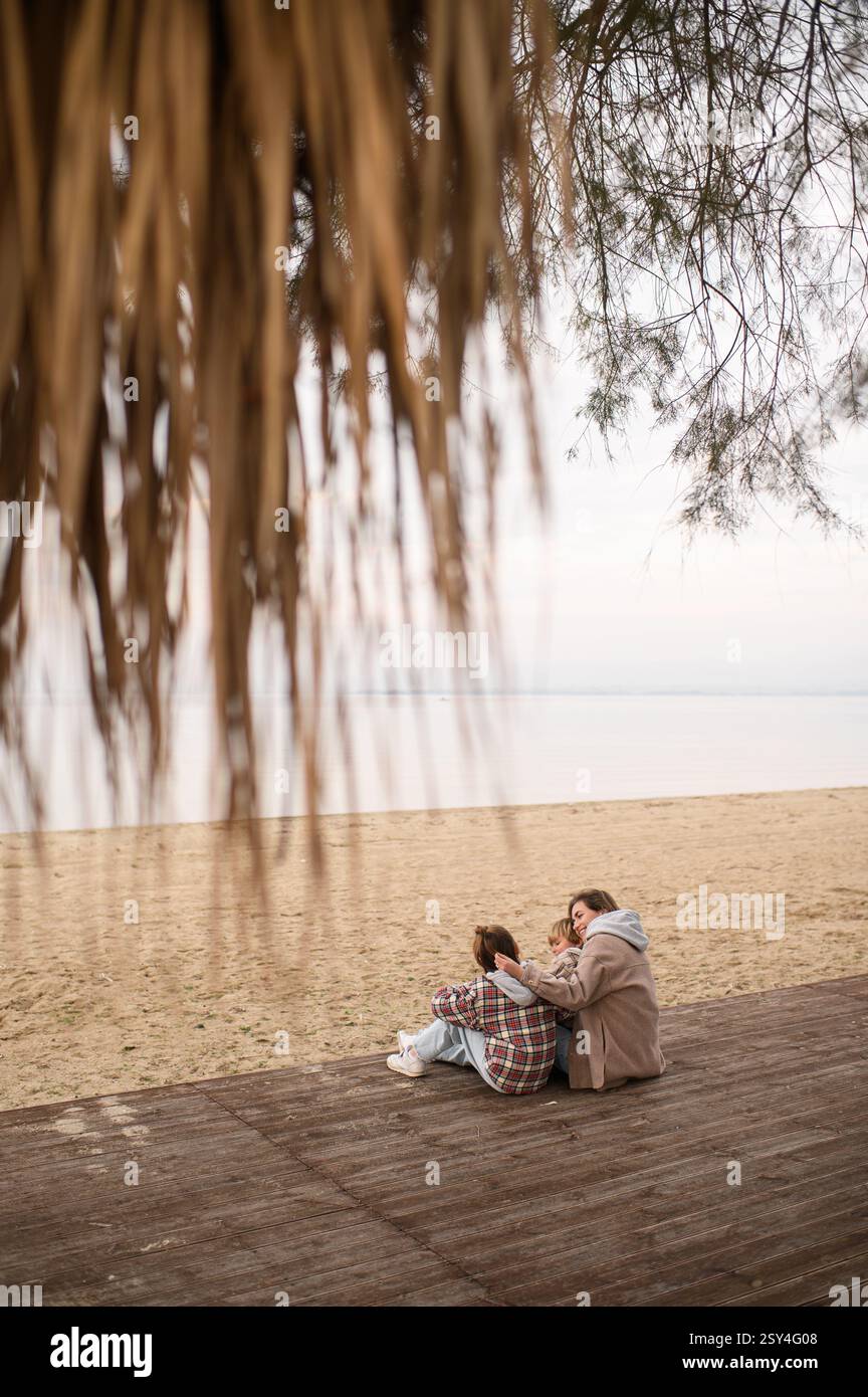 Mutter mit Kindern sitzt am Strand und umarmt sich Stockfoto