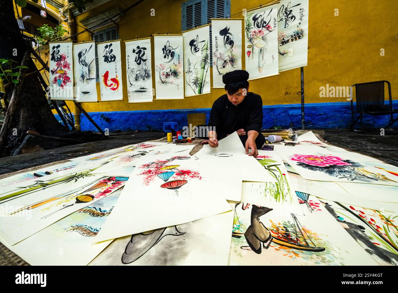 Ein Künstler malt farbenfrohe Bilder mit alten chinesischen Schriftzeichen auf einem Fußweg in Hoi an, Hội an. Stockfoto