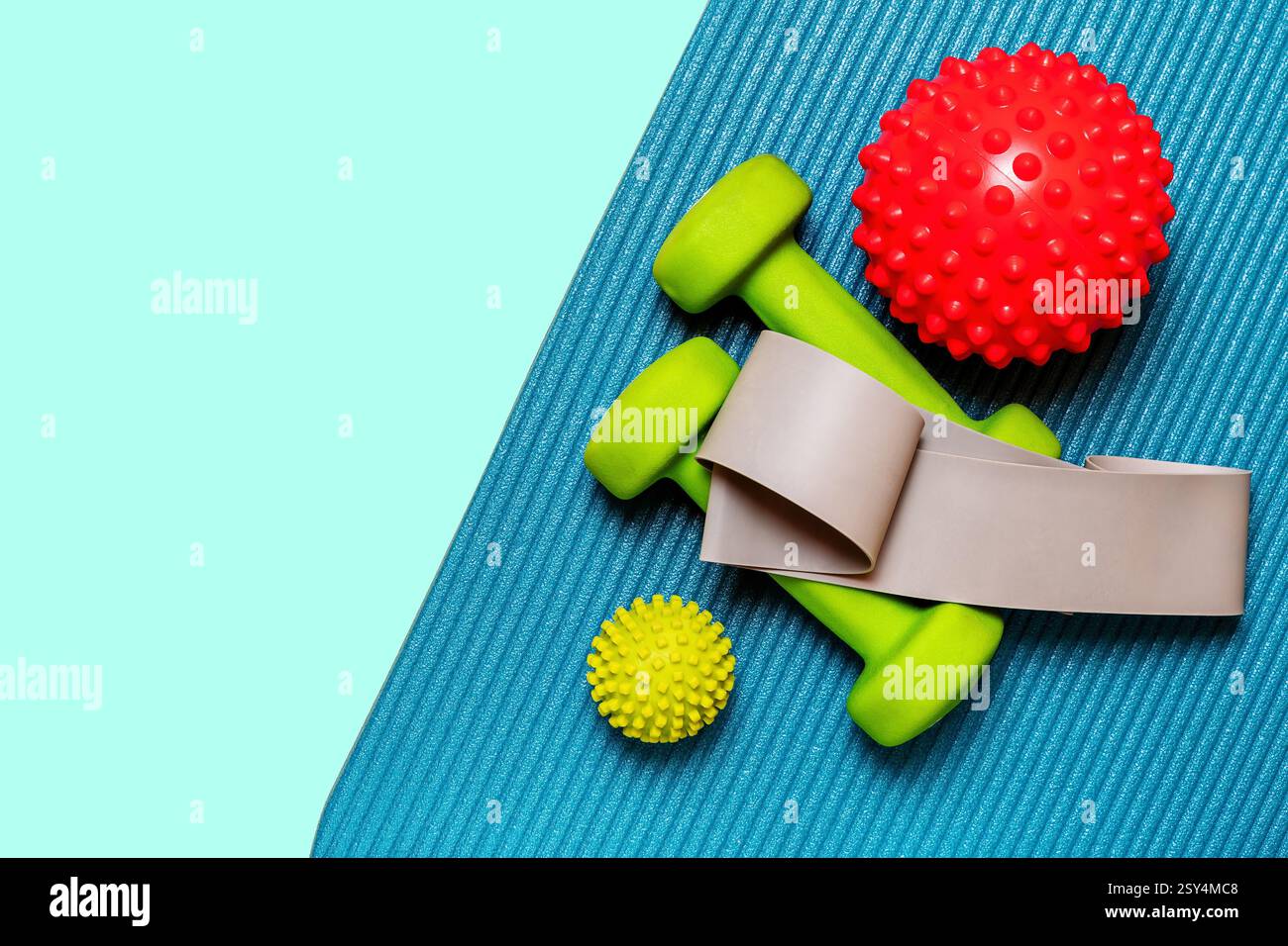 Lebendiger flacher Lay mit einem Paar lindgrünen Kurzhanteln, einem Widerstandsband und zwei spitzen Massagekugeln, die auf einer blaugrünen Yogamatte angeordnet sind Stockfoto