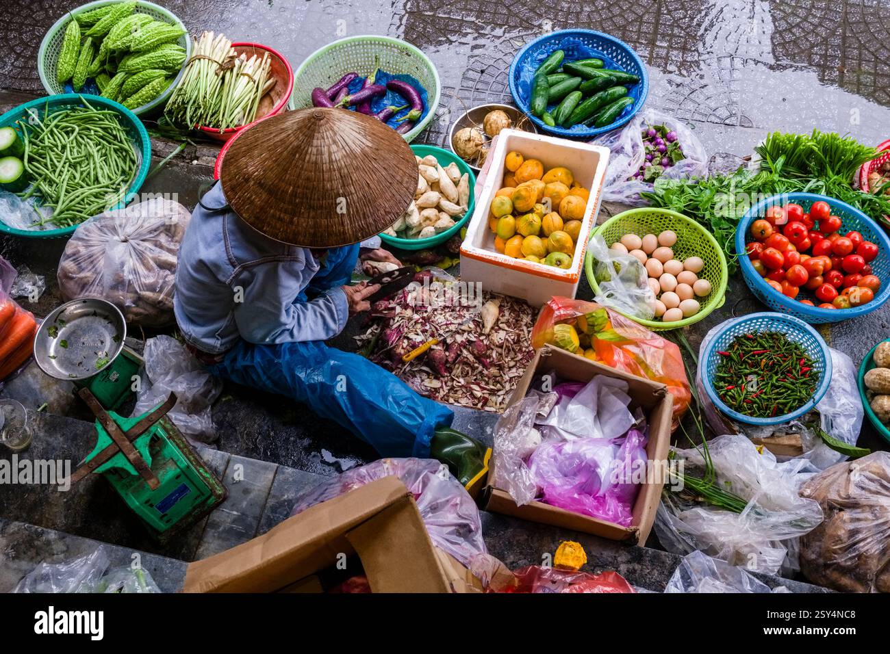 Eine Frau mit konischem Hut verkauft verschiedene Obst- und Gemüsesorten auf einem der vielen Straßenmärkte im Zentrum von Hoi an, Hội an. Stockfoto