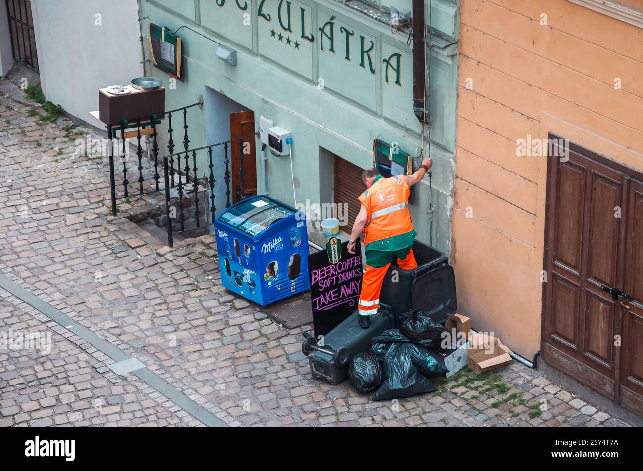 Prag, Tschechische Republik - 12. Juni 2016: Ein Sanitärangestellter in gut sichtbarer Kleidung sammelt Müll aus einem Abfalleimer auf einer kopfsteingepflasterten Straße in der Nähe eines Sho Stockfoto