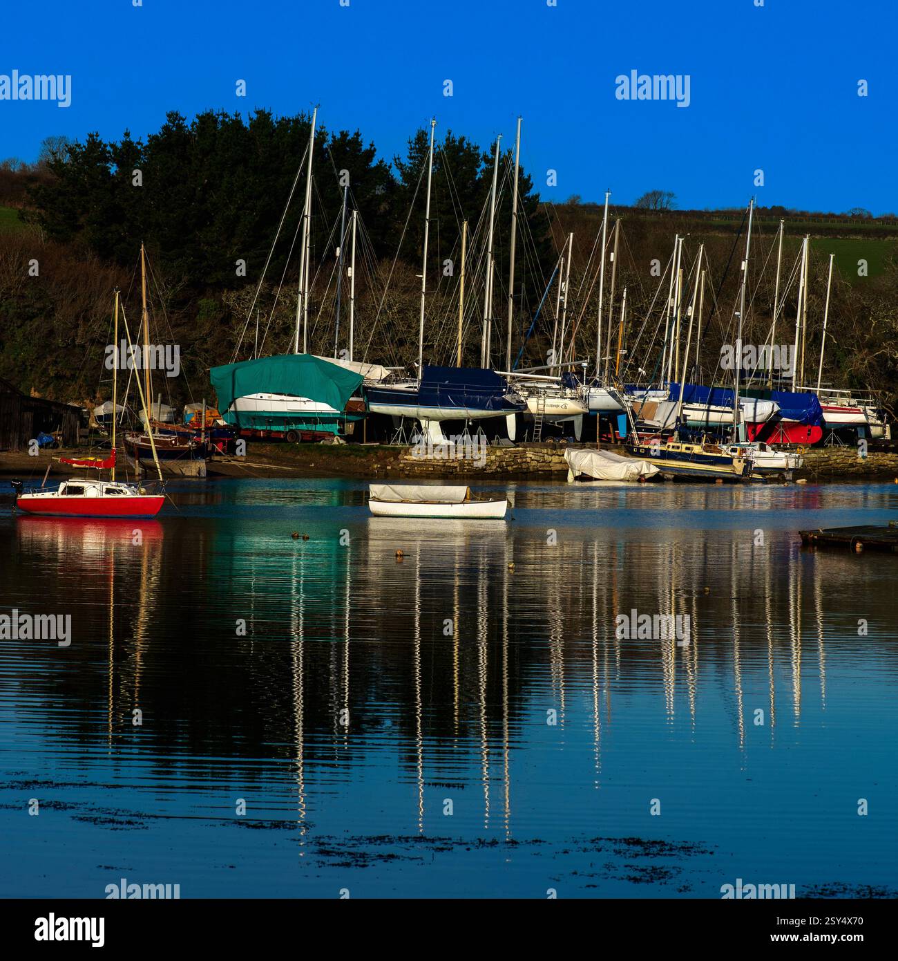 Im Dezember weht eine leichte Brise sanft die Oberfläche des St Just Creek in Roseland, Cornwall, England, da sie die Masten von Yachten reflektiert, die für den Winter in einer Werft aufgestellt wurden. Der Tidal Roseland Peninsula Creek ist ein Einlass der Flussmündung des Flusses FAL, der zu den Carrick Roads und dem offenen Meer führt. Stockfoto