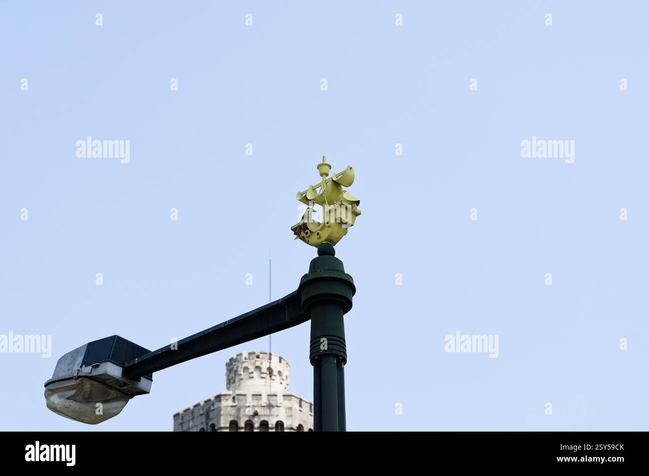 Ein gelbes Schiffswappen auf einem Laternenpfahl mit einem historischen Steinturm im Hintergrund Stockfoto