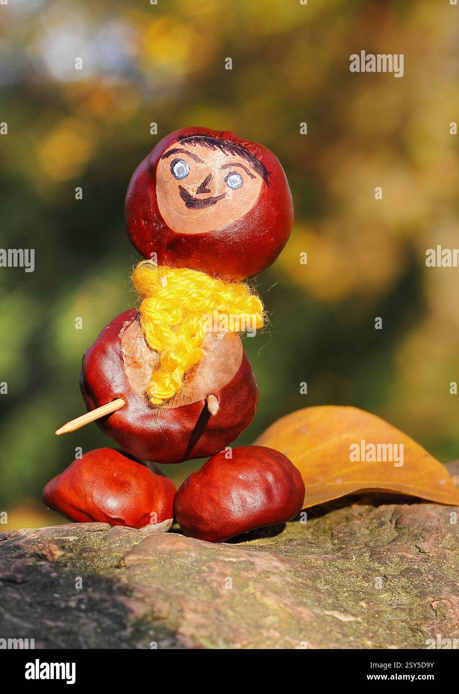 Lustige Kastanienfigur mit rotem Hut und gelbem Schal auf einem Baumstamm Stockfoto