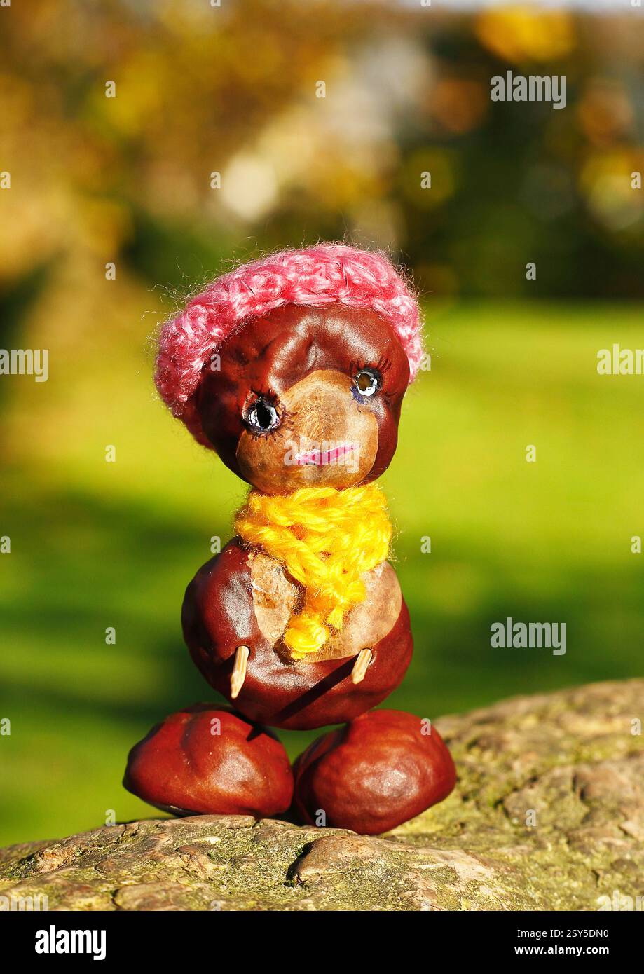 Lustige Kastanienfigur mit rotem Hut und gelbem Schal auf einem Baumstamm Stockfoto