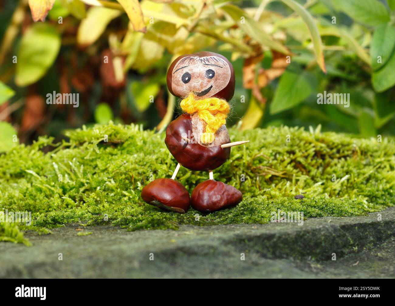 Lustige Kastanienfigur mit gelbem Schal auf Moos Stockfoto