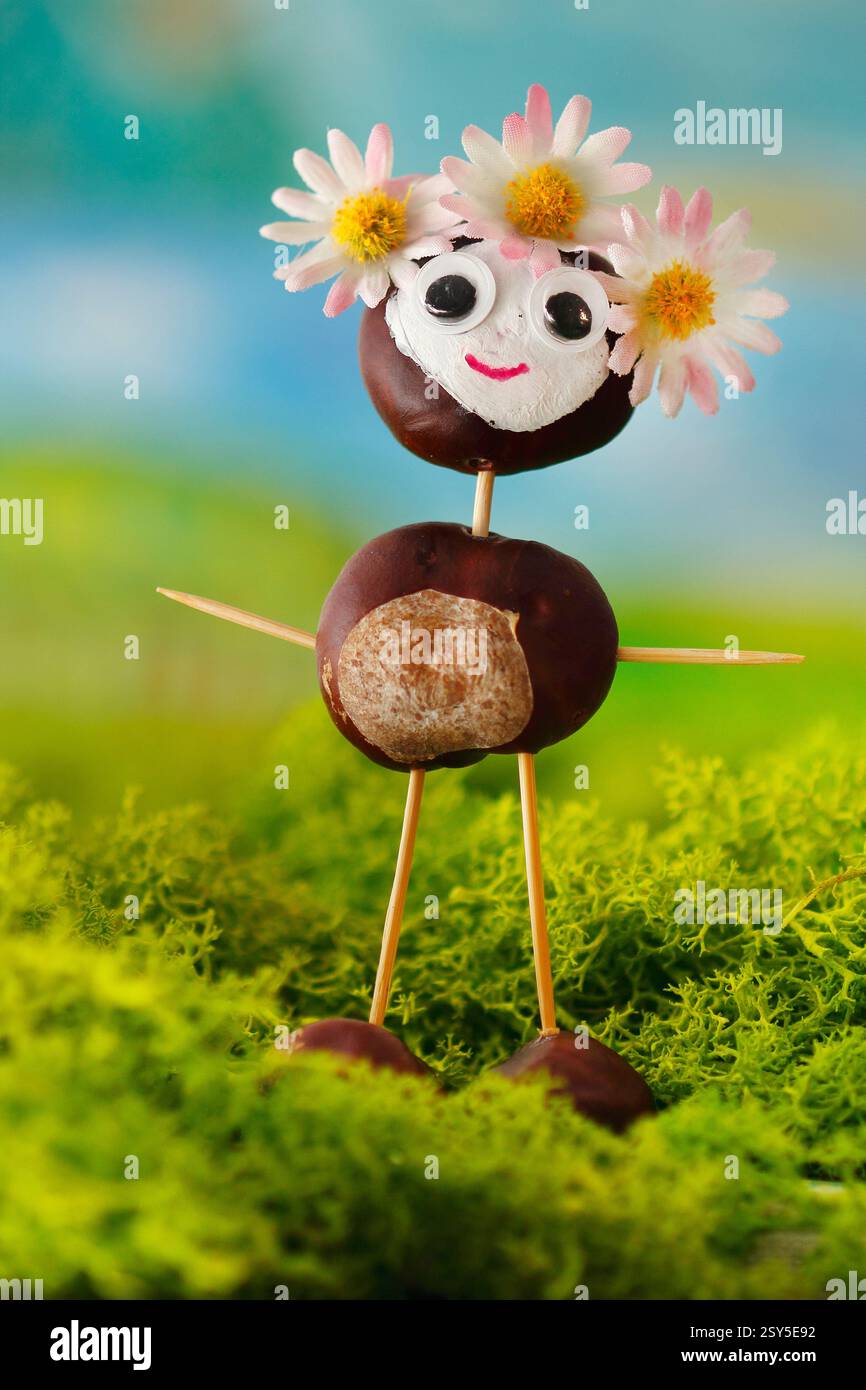 Lustige Kastanienfigur mit Haarkranz und schönen Augen, die auf Moos stehen Stockfoto
