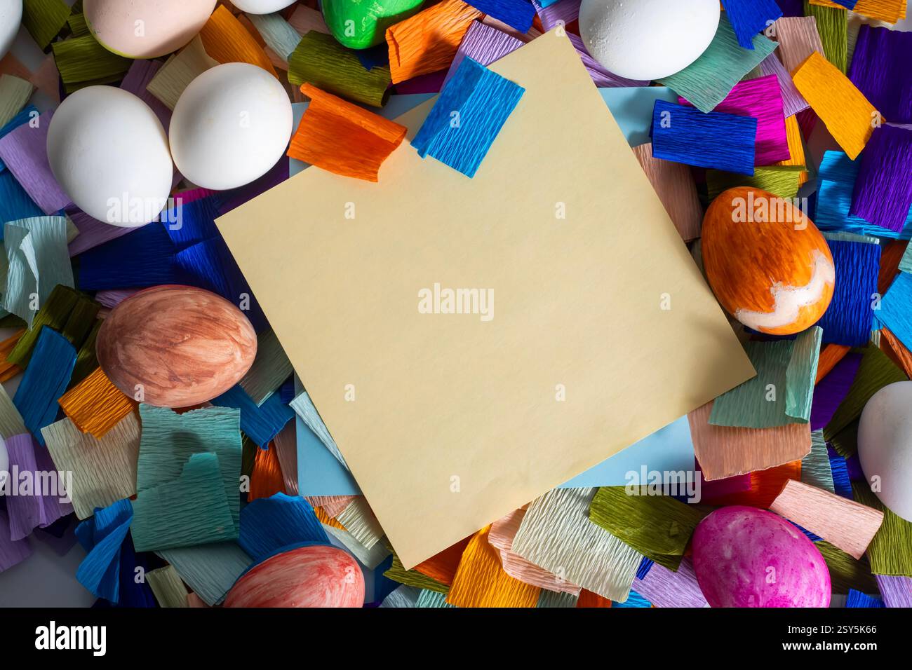 Ein leeres gelbes Notizbuch, umgeben von bunten Eiern und lebhaften Papierstücken für die Osterfeier. Stockfoto