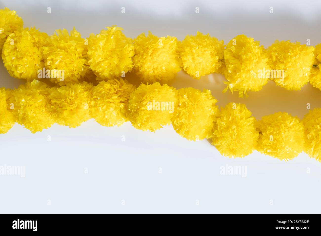 Wunderschön verzierte helle gelbe dekorative künstliche Blumengirlande auf weißem Hintergrund. Perfekt, um festlichen Dekoraten einen verspielten Touch zu verleihen Stockfoto