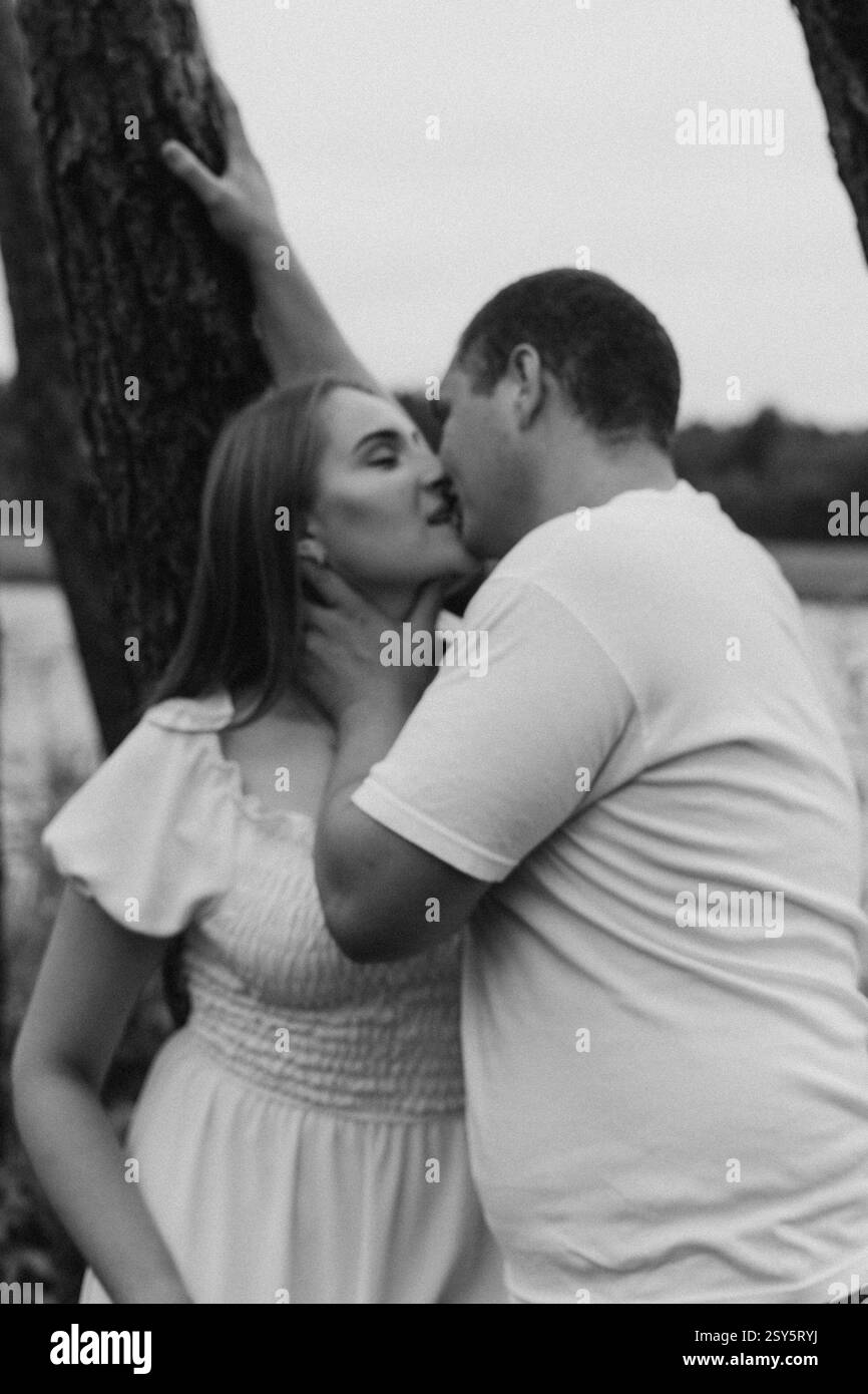 Romantisches Paar, das sich an einem bewölkten Tag in der Nähe eines Sees und eines Waldes küsst und umgibt. Stockfoto