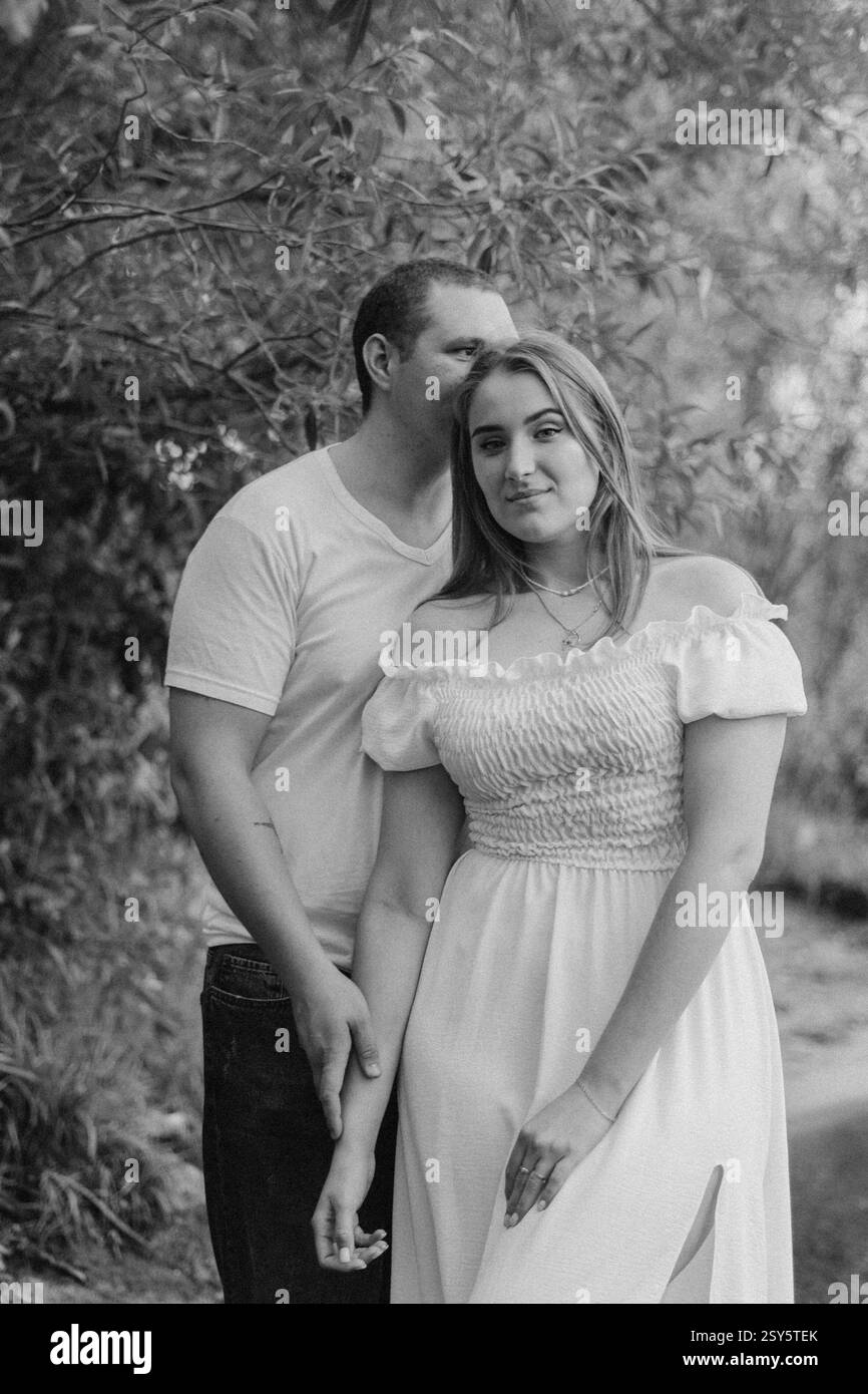 Romantisches Paar, das sich an einem bewölkten Tag in der Nähe eines Sees und eines Waldes küsst und umgibt. Stockfoto