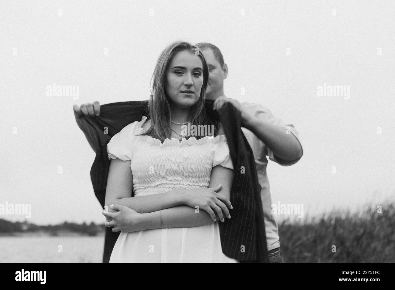 Romantisches Paar, das sich an einem bewölkten Tag in der Nähe eines Sees und eines Waldes küsst und umgibt. Stockfoto