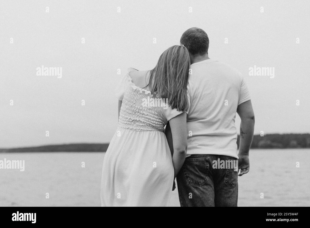 Romantisches Paar, das sich an einem bewölkten Tag in der Nähe eines Sees und eines Waldes küsst und umgibt. Stockfoto