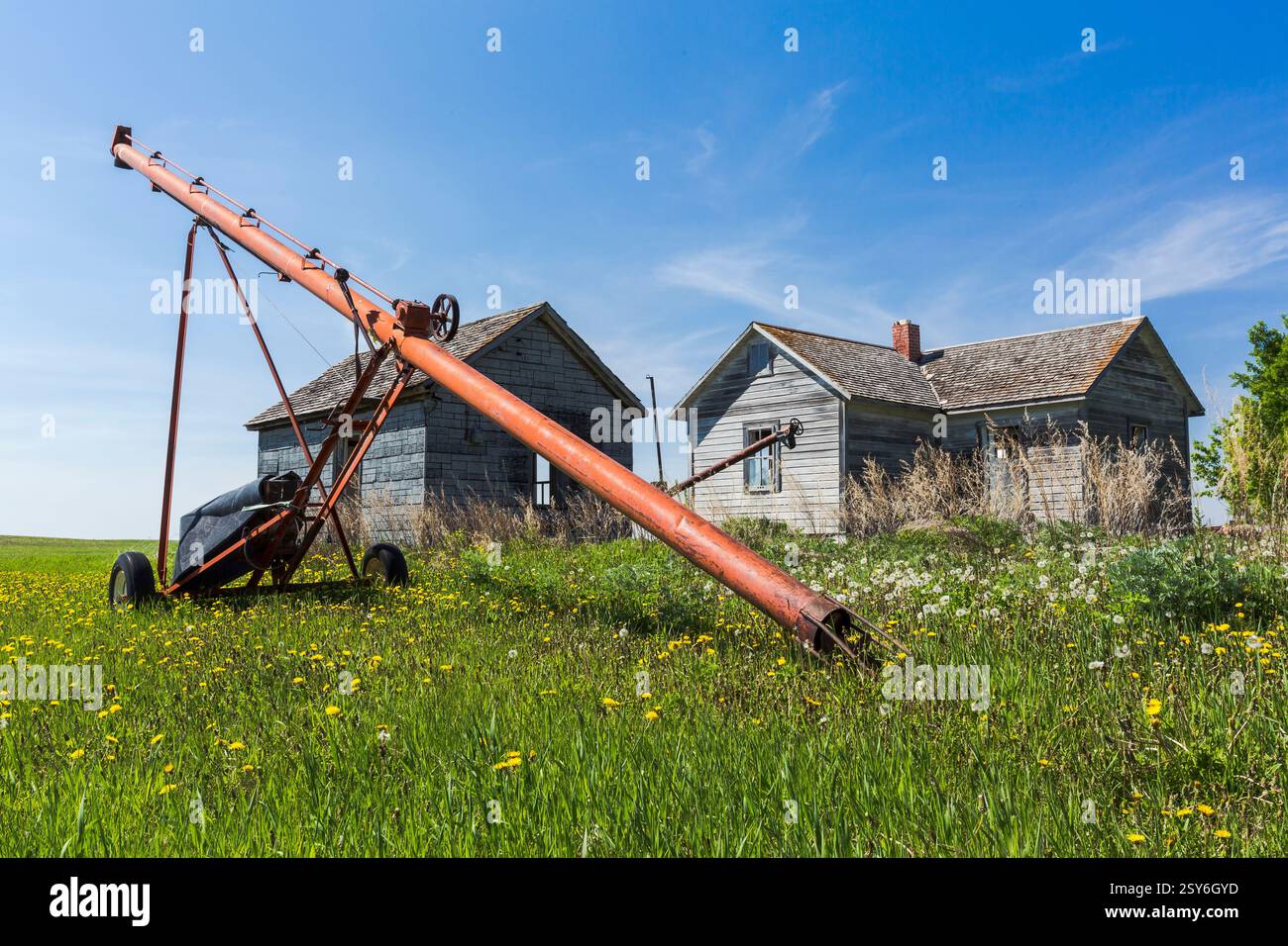 Roter Traktor befindet sich auf einem Feld neben einem Haus. Das Haus ist alt und hat einen Kamin Stockfoto